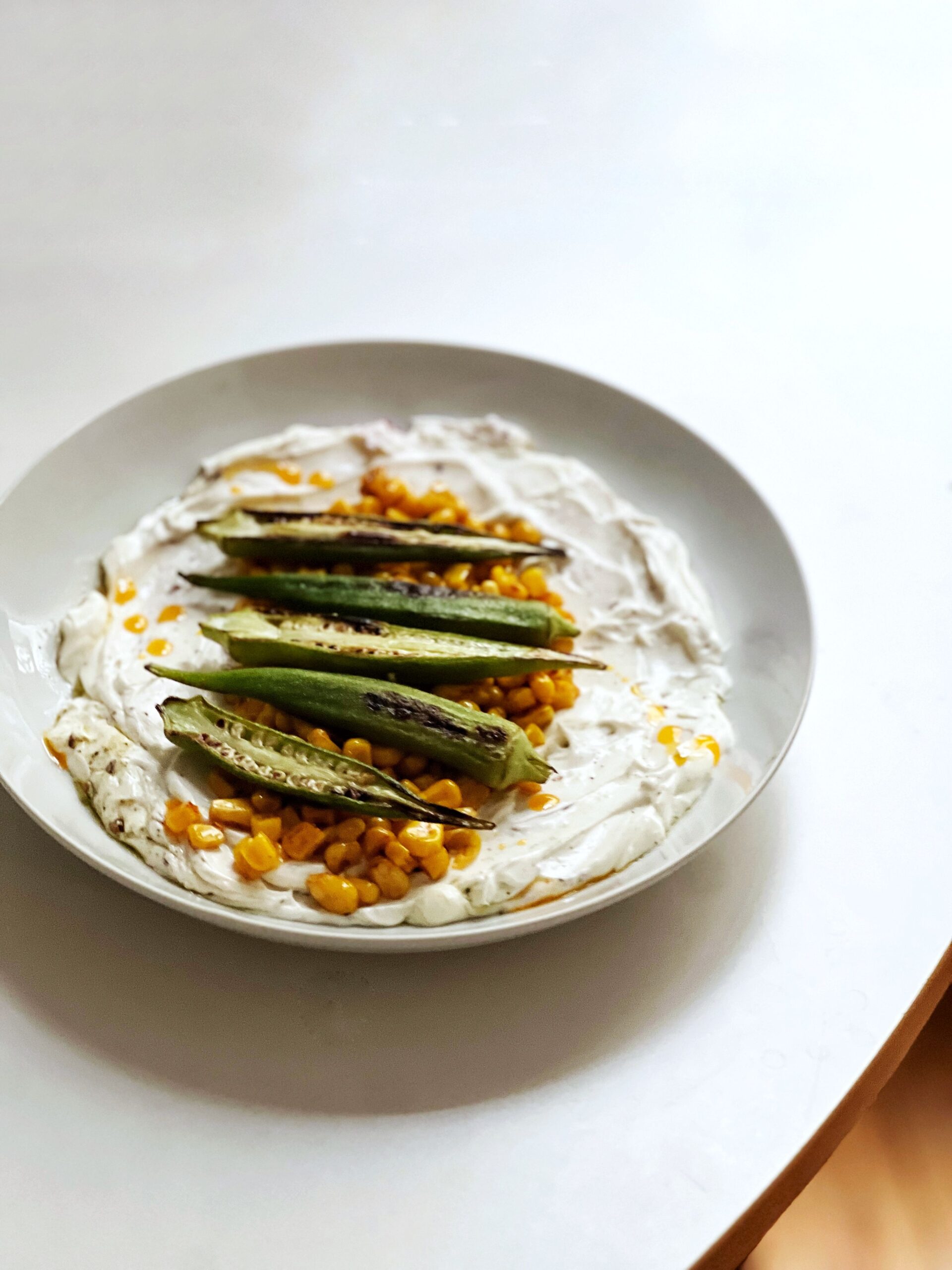 seared okra and charred corn over labneh in a dish on a table
