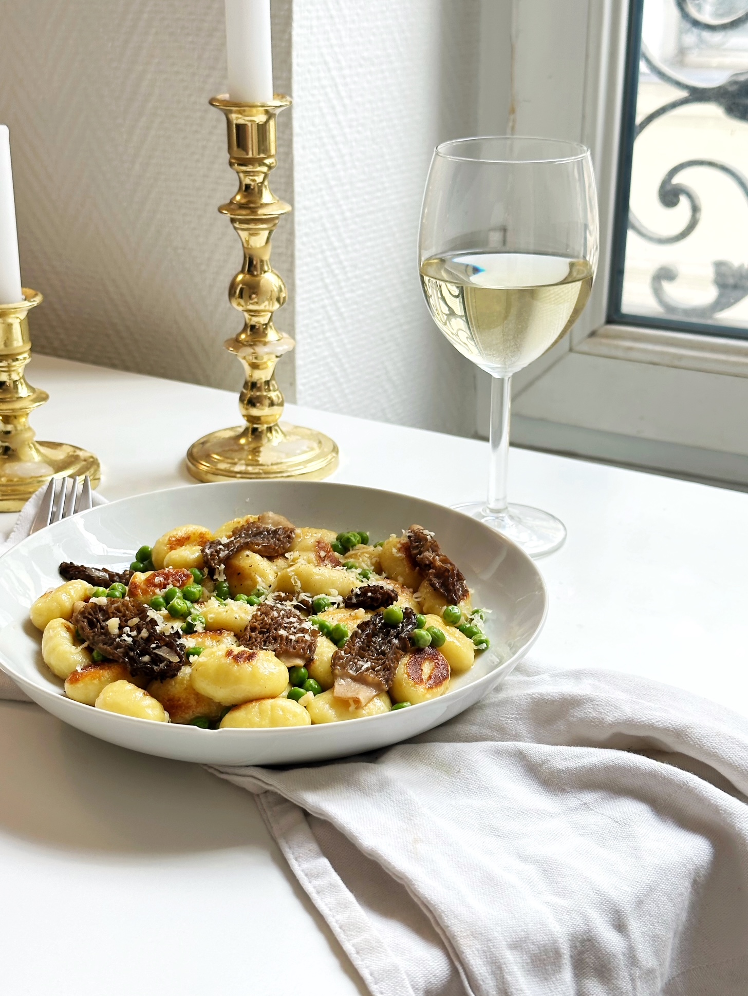 seared gnocchi with morels and english peas and a glass of white wine on an elegant dining table