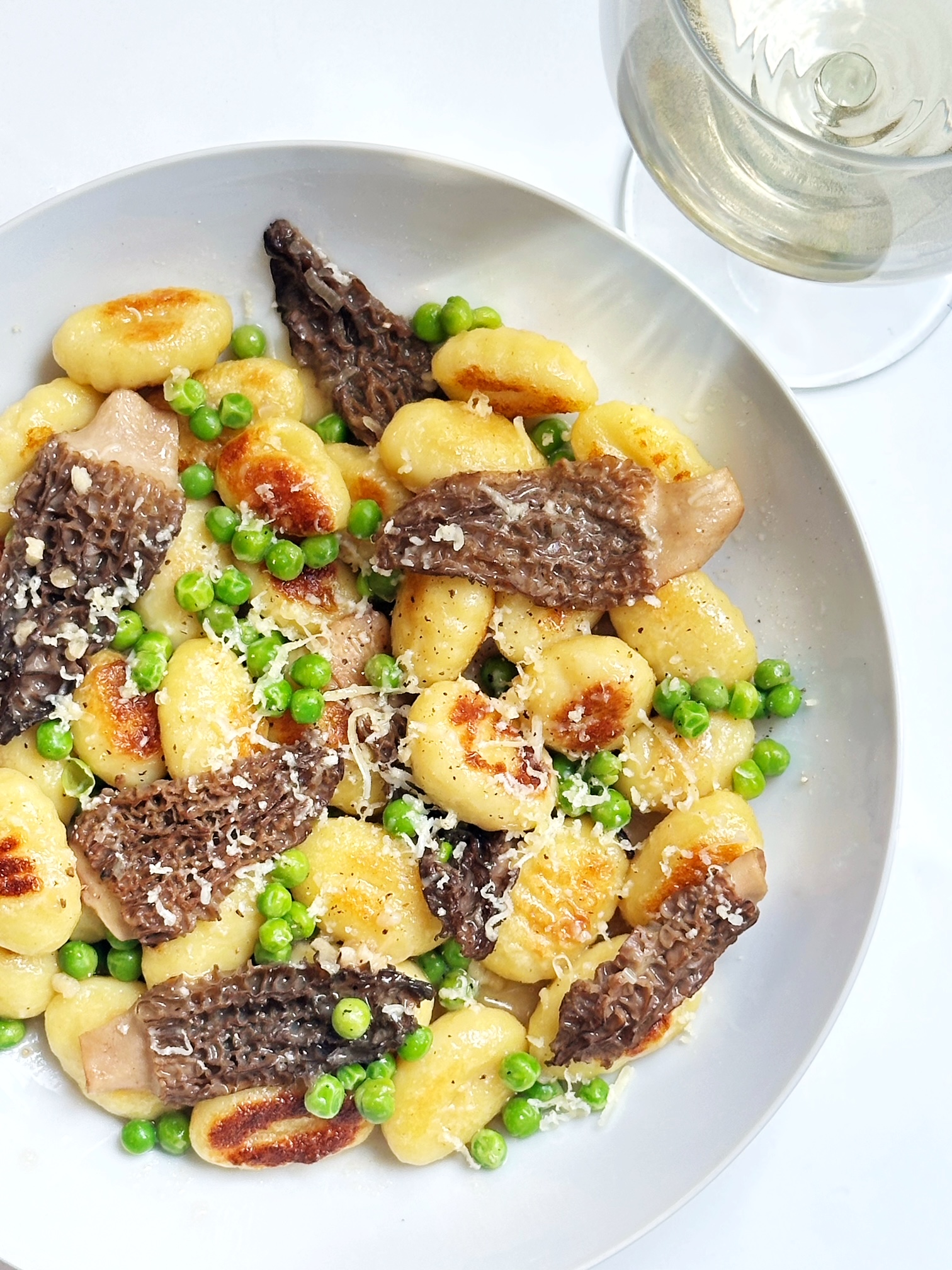 seared gnocchi with morels and english peas in a butter sauce with a glass of white wine